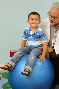 Young boy sitting on balance ball with doctor.