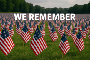 A grassy field with small American flags arranged in rows the whole length of the field. Over the flags, the text We Remember is visible.