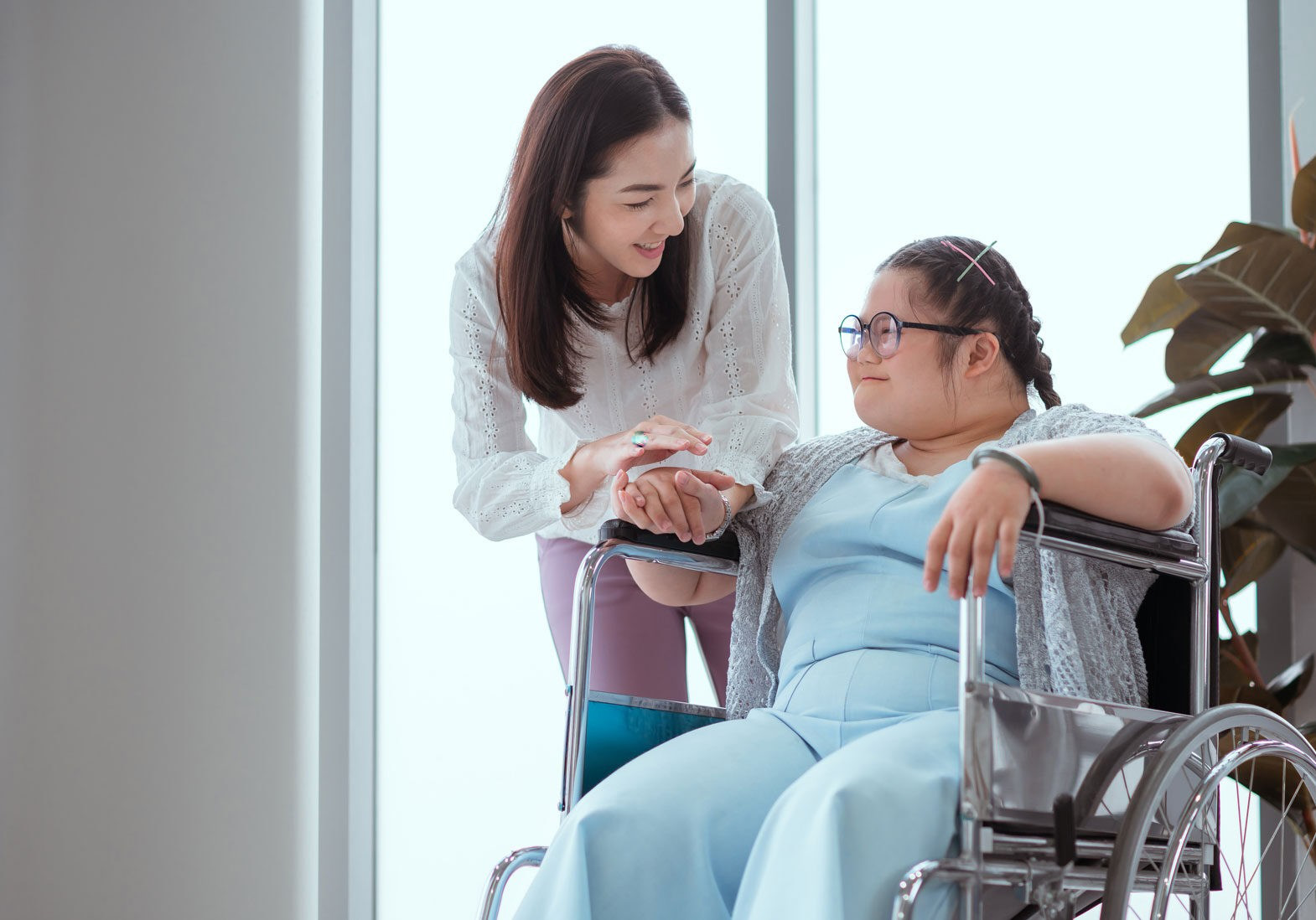 Caregiver bends to warmly greet patient sitting in a wheelchair.